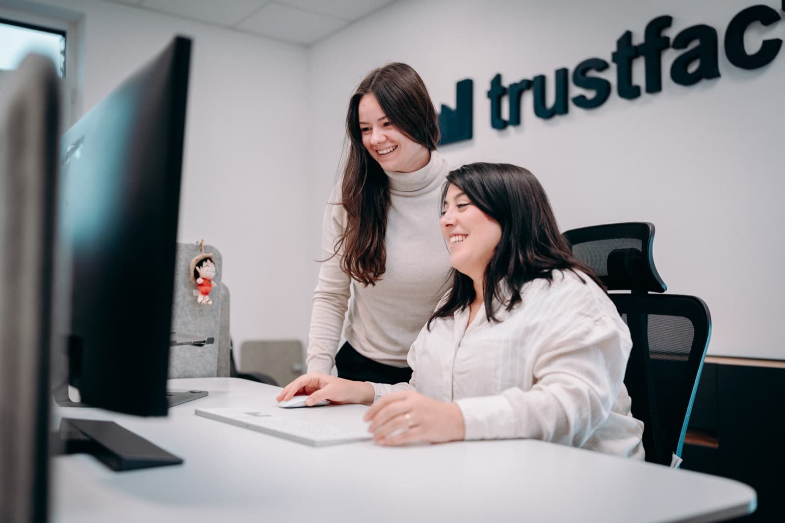 Zwei Trustfactory-Teammitglieder besprechen lächelnd Ergebnisse am Bildschirm